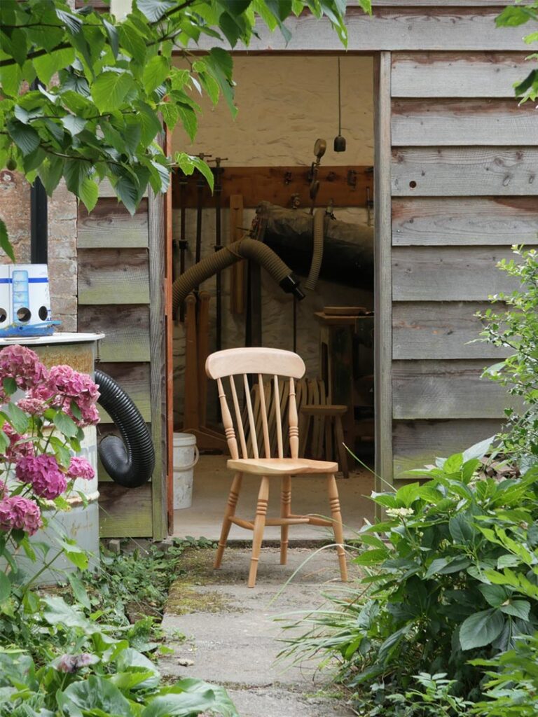 Handmade comb back Windsor dining chair positioned outside a traditional chairmaking workshop.